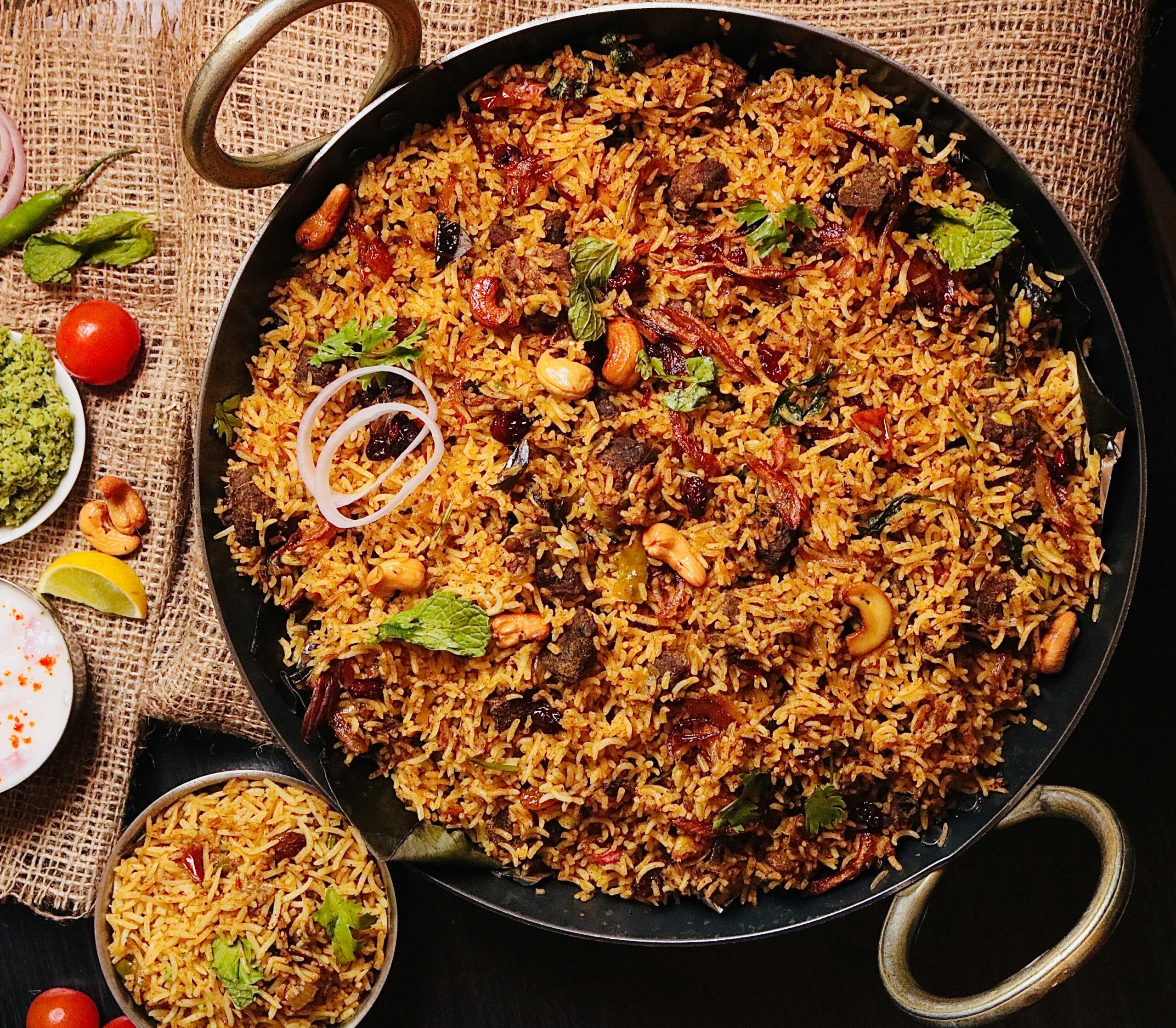 Home Top view of flavorful Indian biryani in a cooking pan, garnished with cashews and herbs.